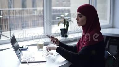一个戴着传统阿拉伯头巾的<strong>可爱女孩</strong>正在她的笔记本电脑上做一些事情，然后把耳机<strong>放</strong>进耳朵里